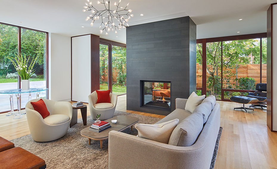 A stunning large scale linear stone veneer adorns a fireplace with a flame in a living room filled with nature and windows